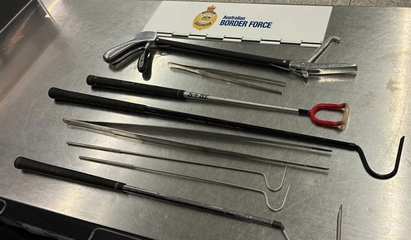 Various metal tools and implements laid out on a gray surface with an "Australian Border Force" sign above.
