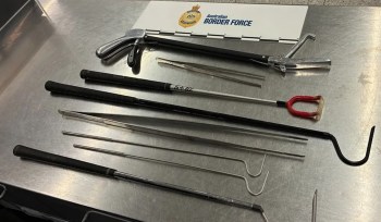 Various metal tools and implements laid out on a gray surface with an "Australian Border Force" sign above.