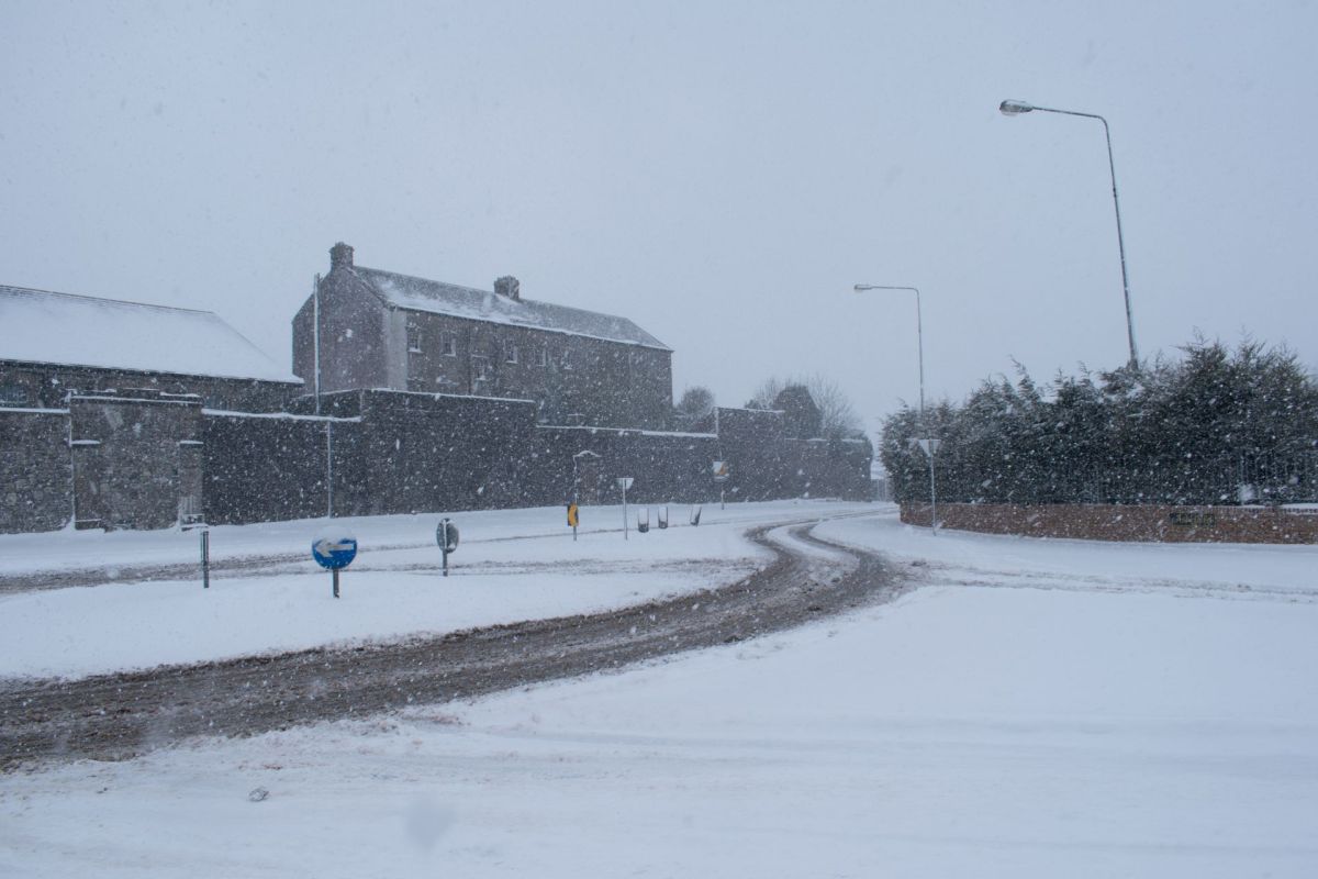 A snow-covered road curves past buildings in a blizzard in Ireland