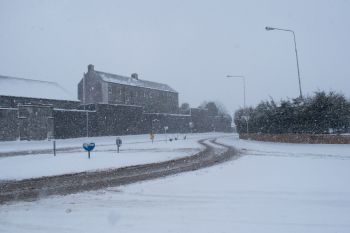 A snow-covered road curves past buildings in a blizzard in Ireland