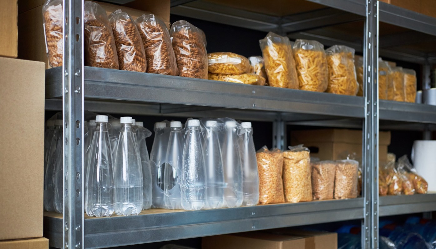 Shelves filled with various bags of pasta, snacks, and bottles of water in a storage area.