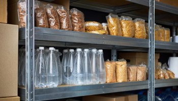 Shelves filled with various bags of pasta, snacks, and bottles of water in a storage area.