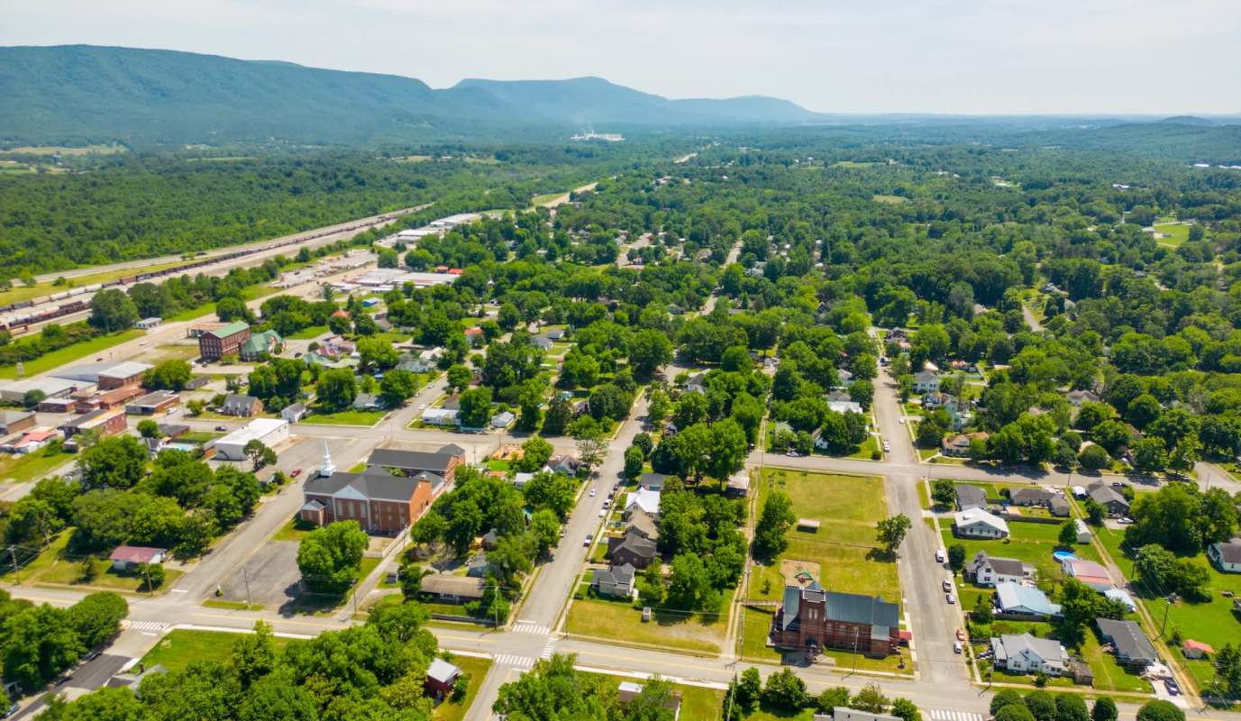 An aerial view of a small town surrounded by greenery and mountains in the background.