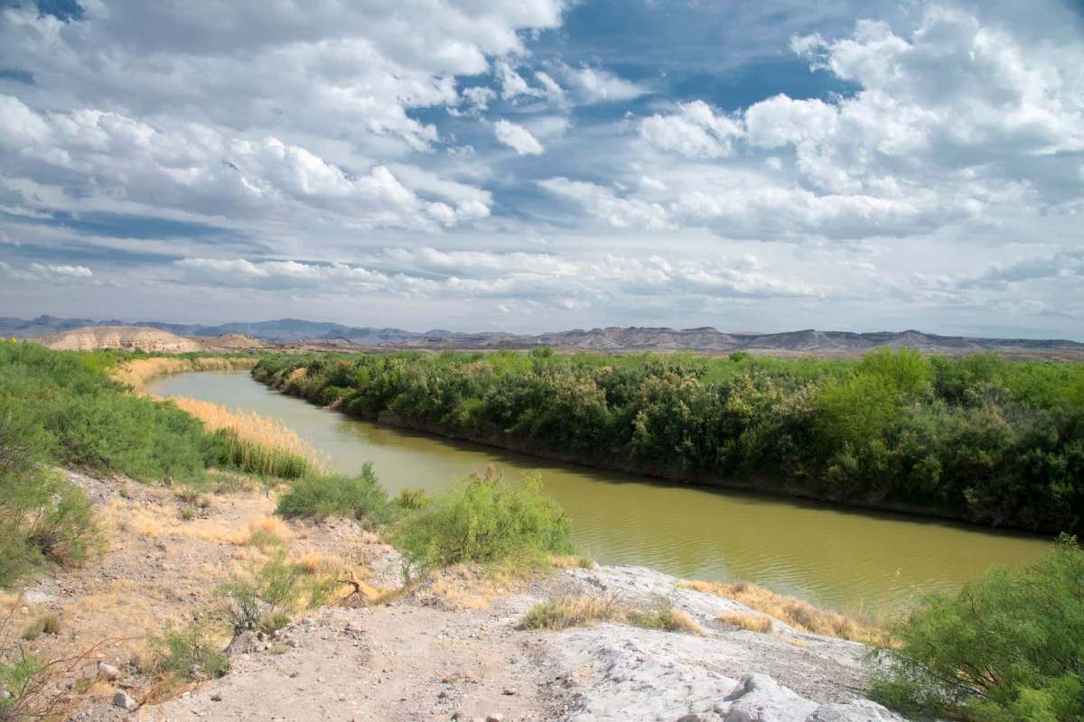 A river winds through a landscape of vegetation and rocky hills under a cloudy sky.