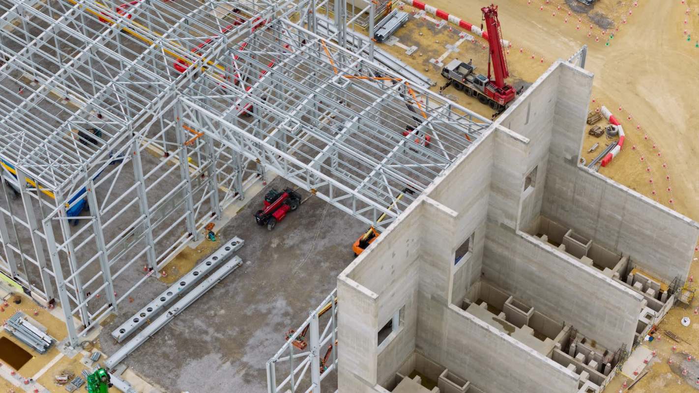 A construction site with metal framing and machinery surrounded by earth and safety barriers.
