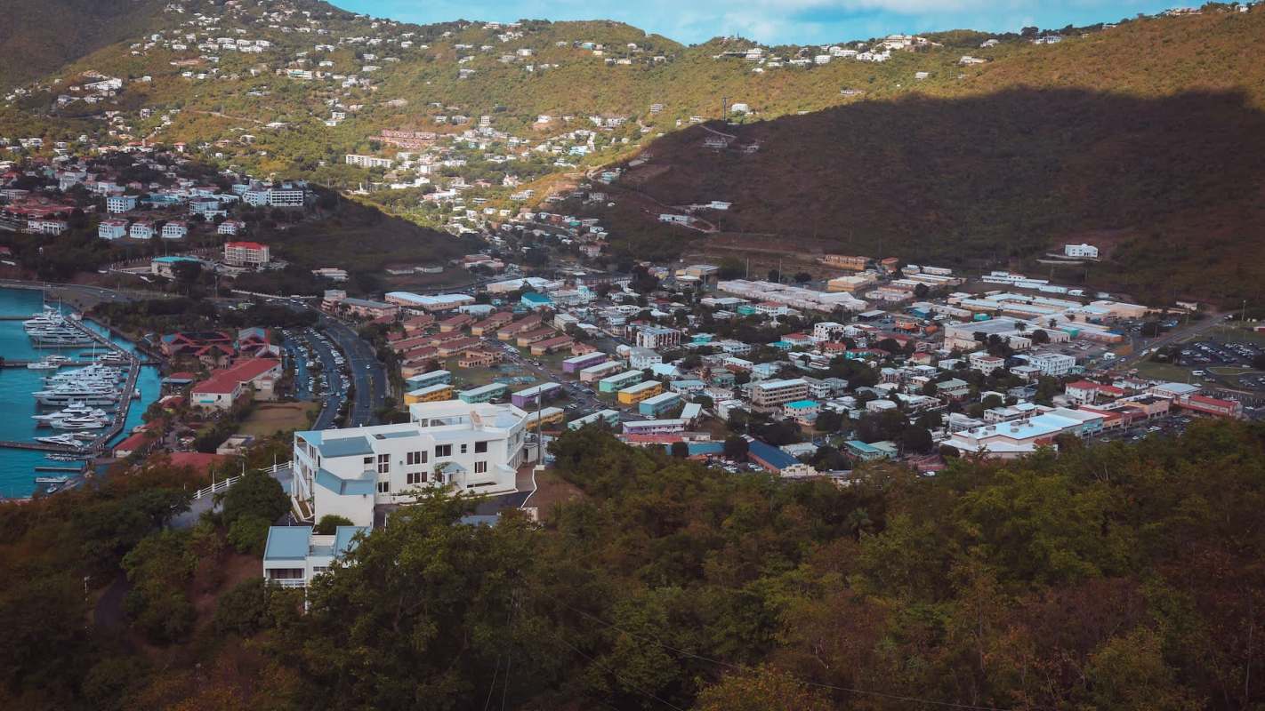 Aerial view of a town in the U.S. Virgin Islands with colorful buildings and a marina along the coast, surrounded by hills.