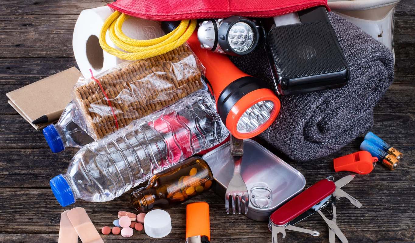 An assortment of emergency supplies, including water bottles, a flashlight, food, a first aid kit, and a multitool.