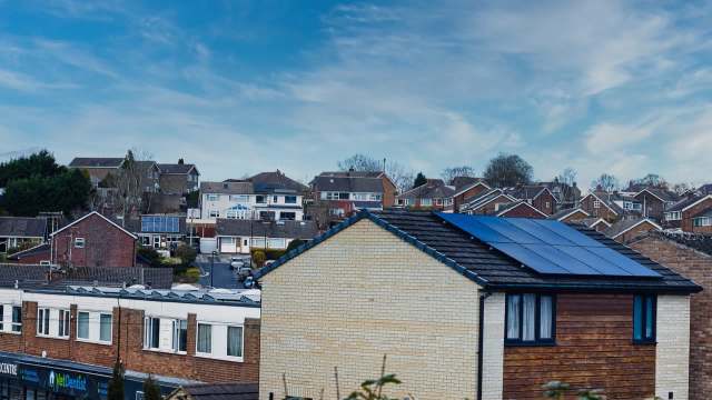 A view of houses in a residential area with solar panels on a roof under a blue sky.
