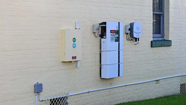 Electrical equipment mounted on a yellow brick wall, including solar inverters and wiring.