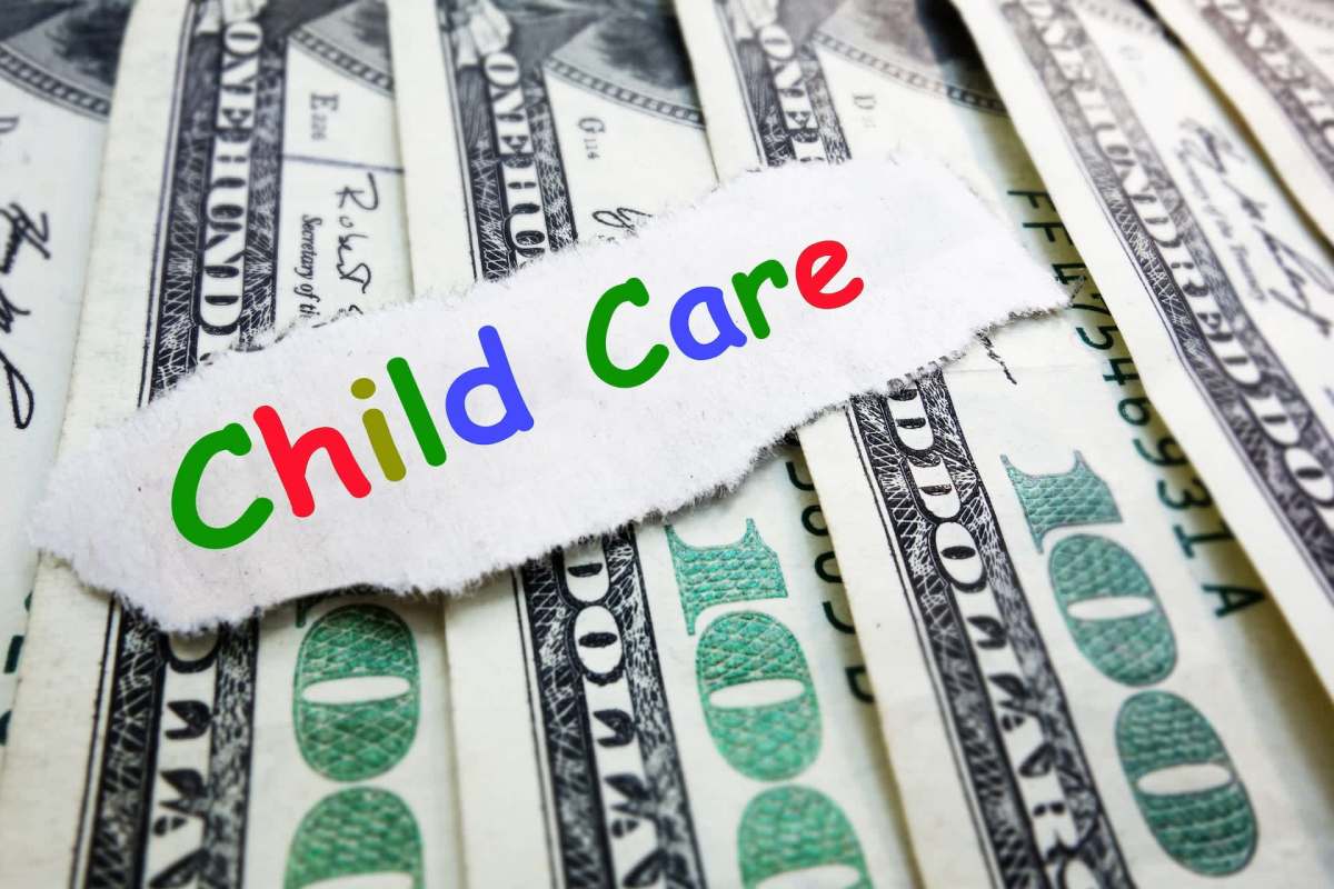 A piece of torn paper with "Child Care" written in colorful letters on top of hundred dollar bills.