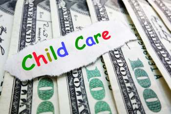 A piece of torn paper with "Child Care" written in colorful letters on top of hundred dollar bills.