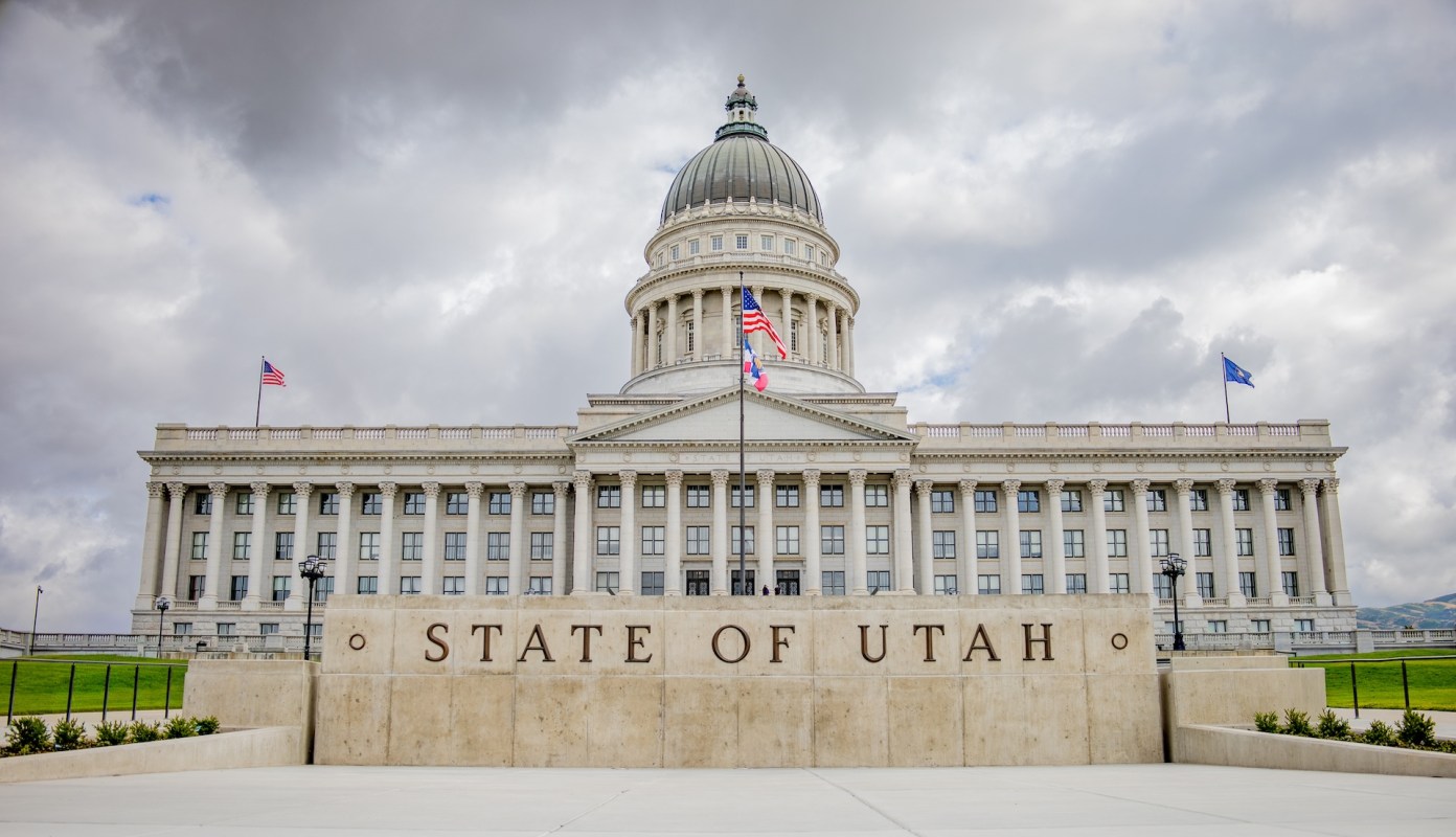 A large stone sign reading "STATE OF UTAH" in front of the Utah State Capitol building.