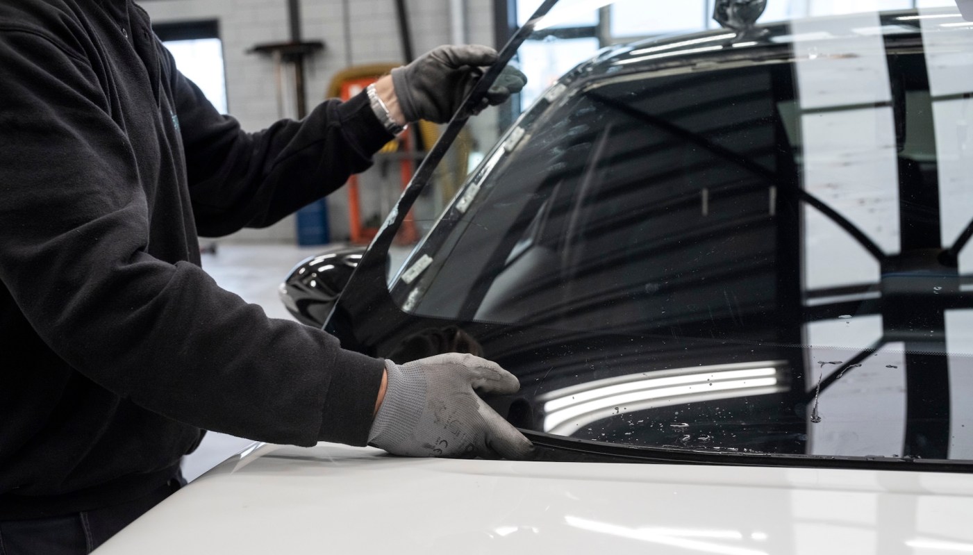 A person installs a car windshield in an automotive workshop.