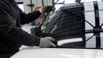 A person installs a car windshield in an automotive workshop.