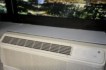 An air conditioning unit placed near a window overlooking a city skyline at night.