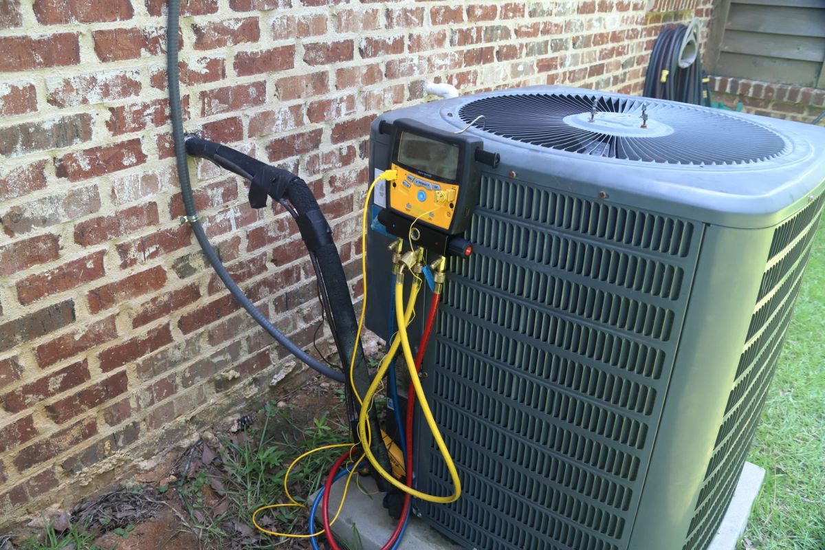 An air conditioning unit with hoses and gauges attached, positioned against a brick wall.