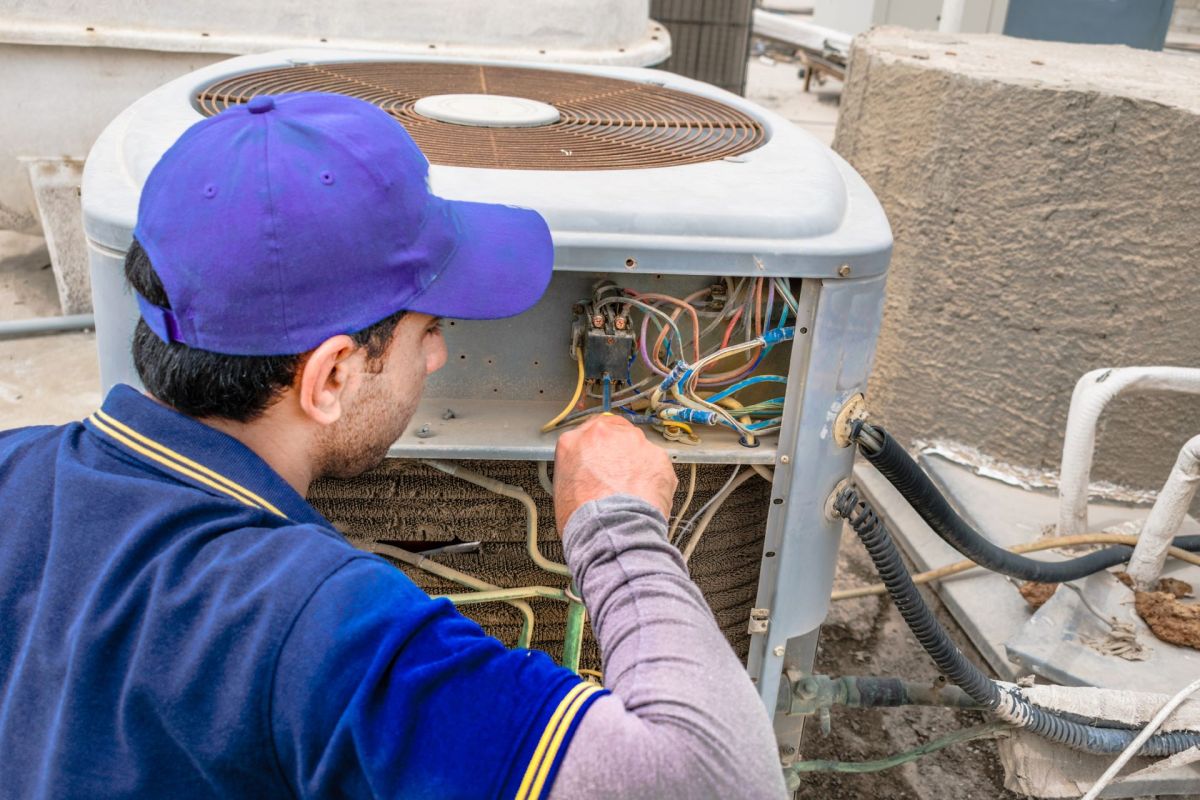A technician works on the electrical connections of an outdoor air conditioning unit.