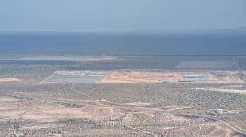 An aerial view of a construction site surrounded by open land and distant mountains.