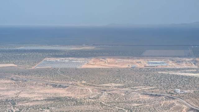 An aerial view of a construction site surrounded by open land and distant mountains.