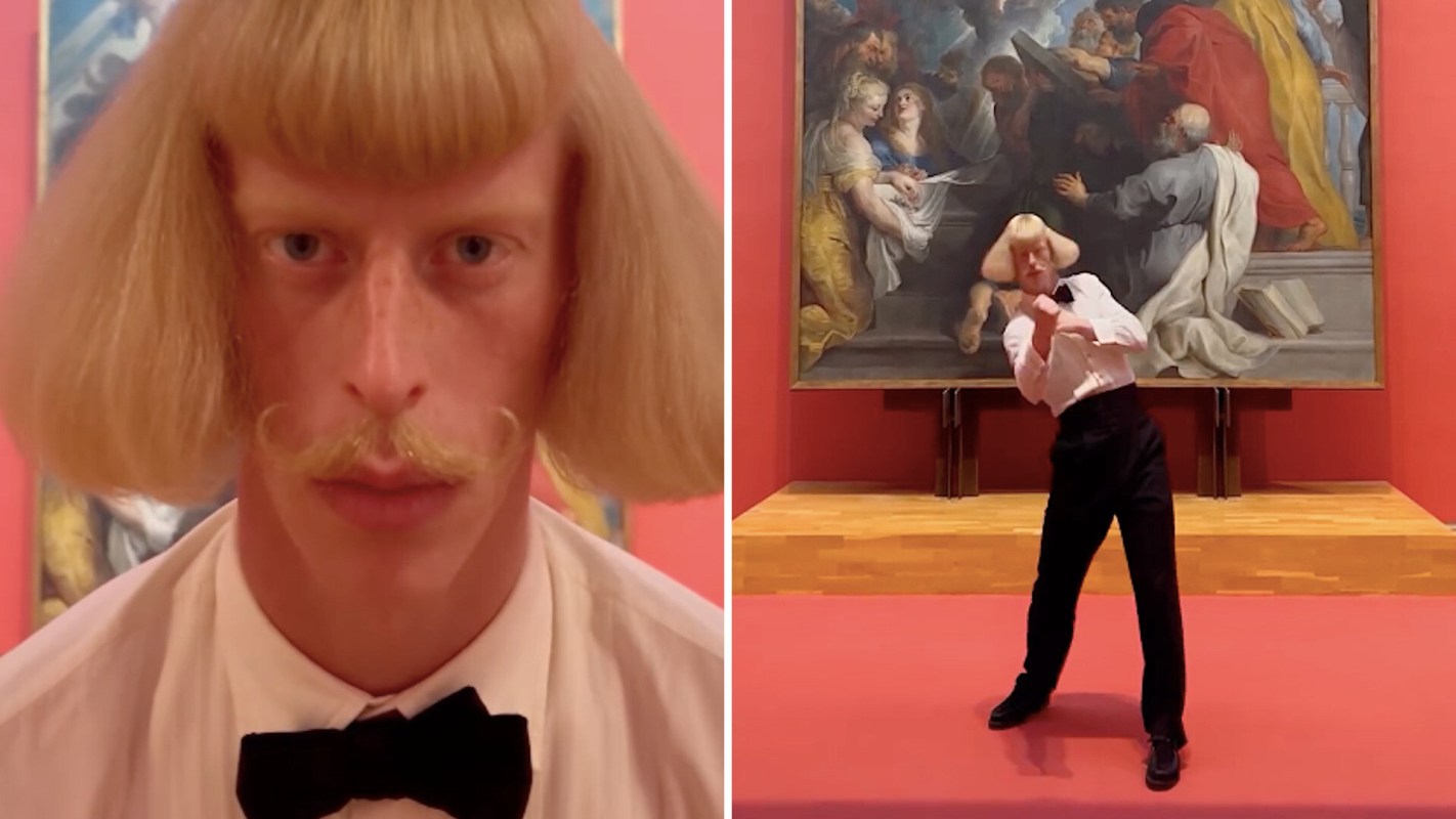 A person with a bowl haircut dances in front of a large painting in a museum.
