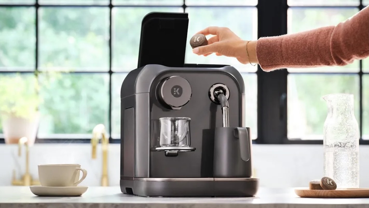 A person places a coffee capsule into a modern coffee machine on a kitchen counter.