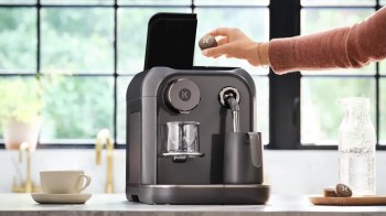 A person places a coffee capsule into a modern coffee machine on a kitchen counter.