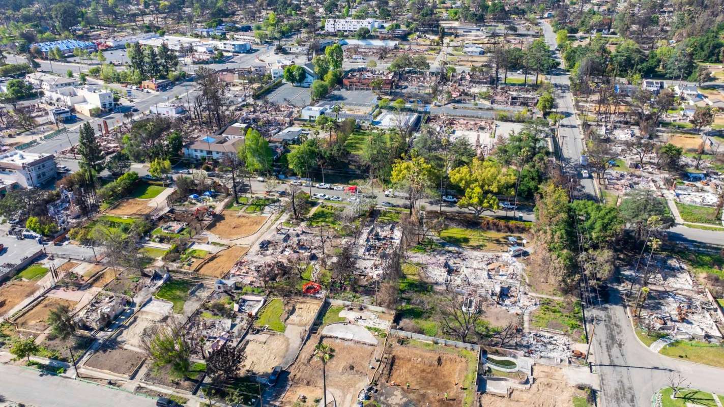 An aerial view of an Altadena, California, neighborhood showing damaged homes alongside intact structures and roads.