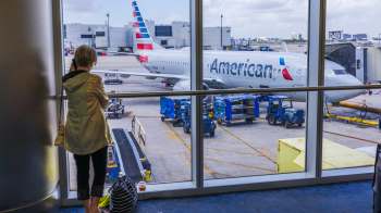 A person on a phone looking through an airport window to an American Airlines plane.