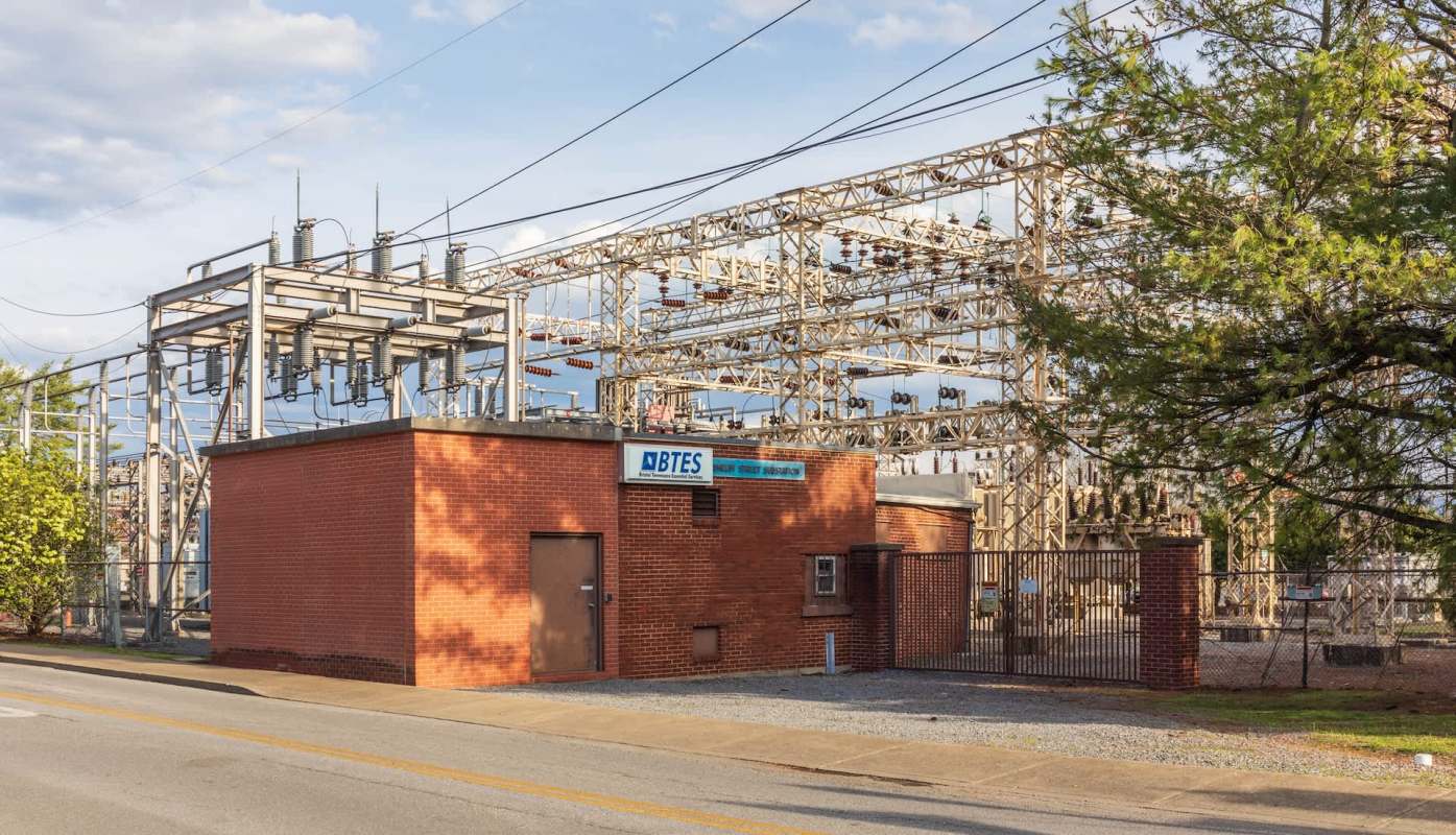 A brick building next to a large electrical substation surrounded by fences and power lines.