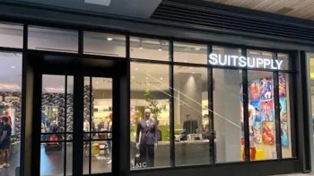 A storefront of a clothing store named "SUITSUPPLY" featuring a mannequin in a suit and colorful displays inside.