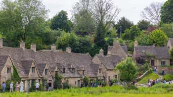 A line of cottages in Arlington Row in Bibury, England, with visitors walking along a path in a green landscape.