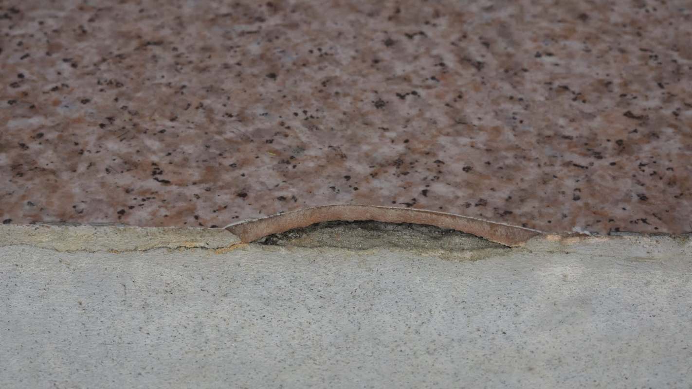 A cracked asbestos tile where a patterned slab meets a concrete base.