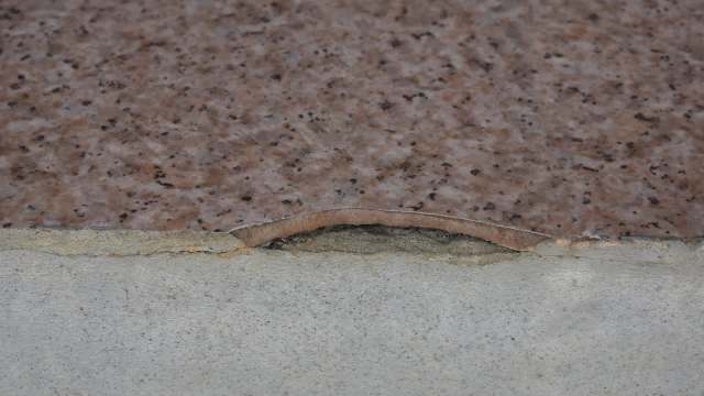 A cracked asbestos tile where a patterned slab meets a concrete base.
