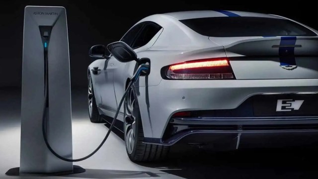 An electric car is plugged into an Aston Martin charging station in a dark setting.