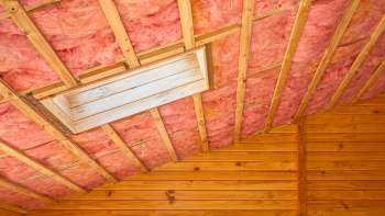 A wooden ceiling with pink insulation and a square opening in the center.