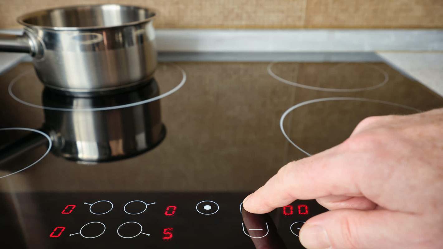 A hand adjusts the controls of an induction cooktop with a metal pot on it.