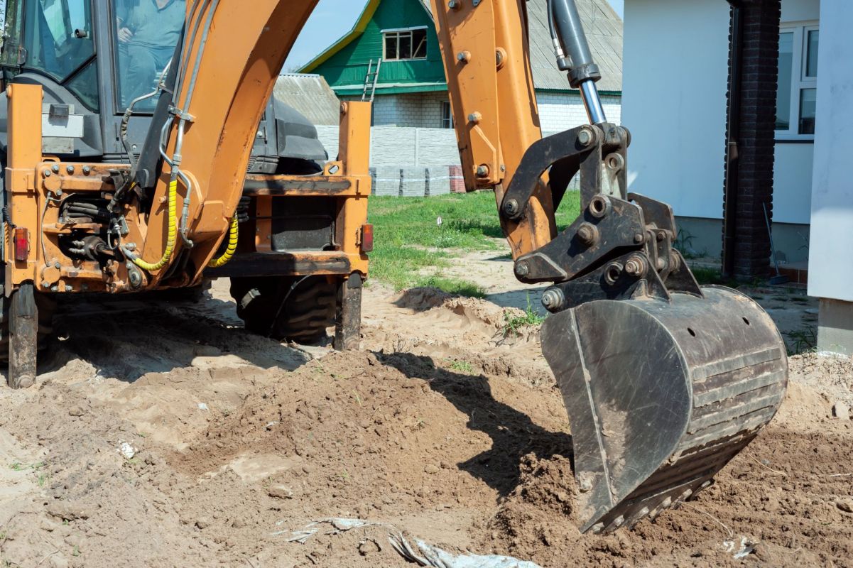 A construction excavator digs into the soil near a building site.