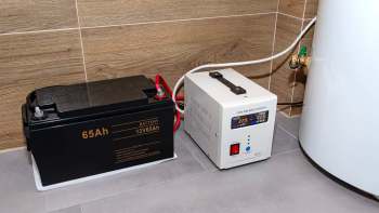 A battery and a pure sine wave inverter connected by cables in a room with tiled flooring.
