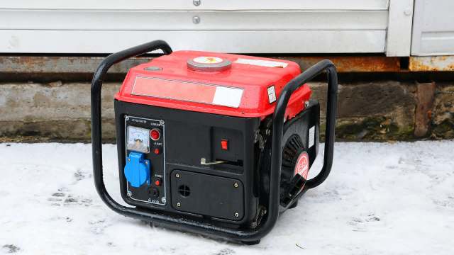 A red and black portable generator sitting on a snowy surface.