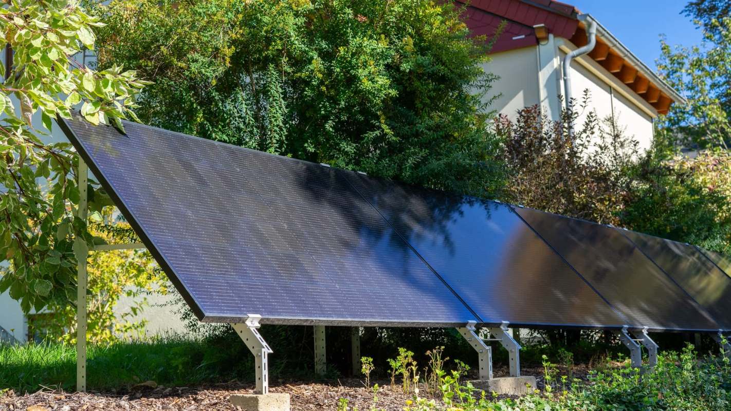 A solar panel installation among greenery near a house.