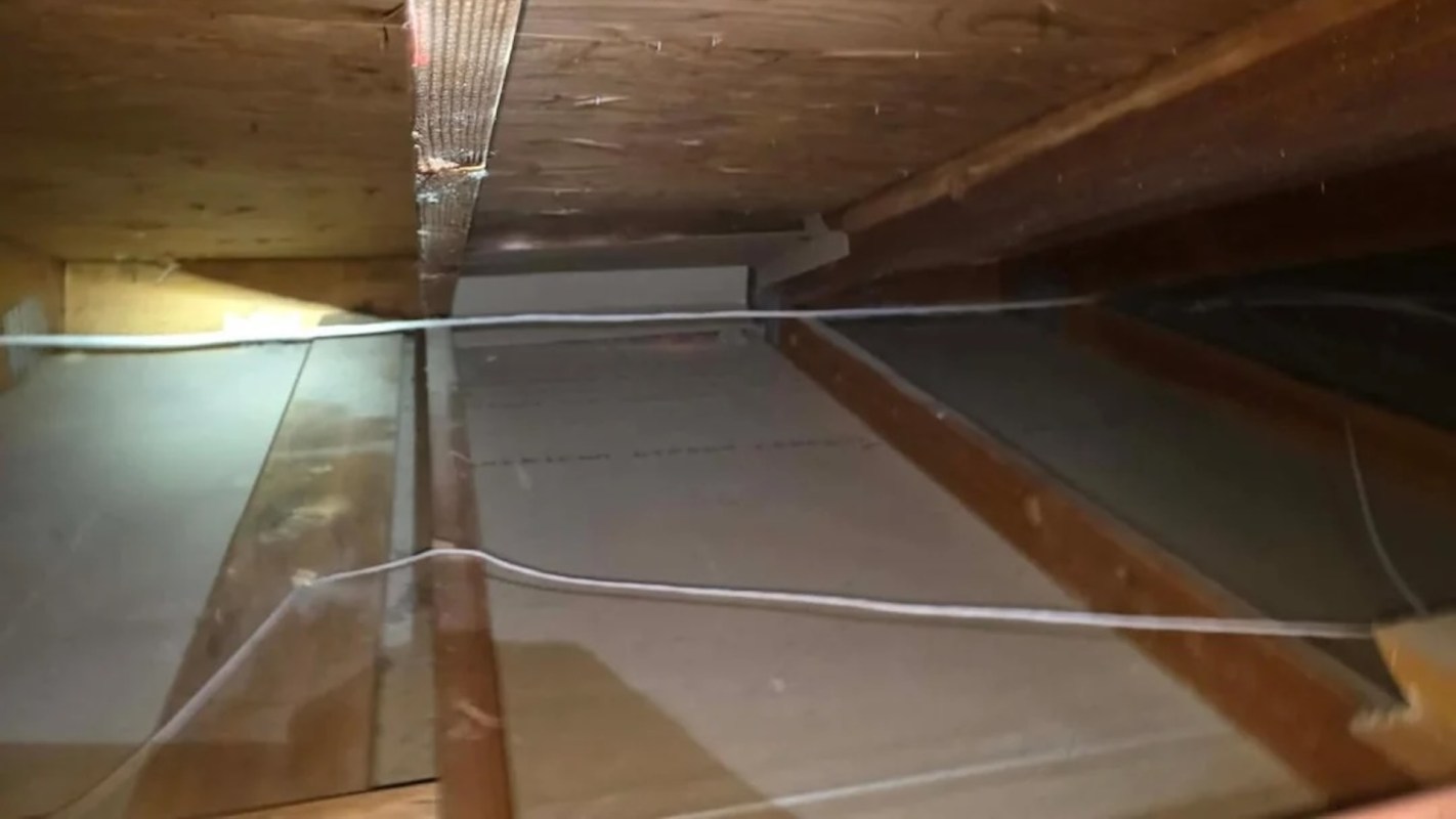 An interior view of an attic with wooden beams and electrical wires.