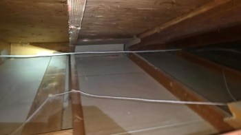 An interior view of an attic with wooden beams and electrical wires.