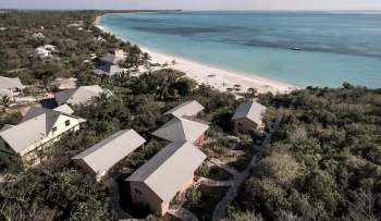 Aerial view of beachside cottages surrounded by greenery and a sandy shoreline.