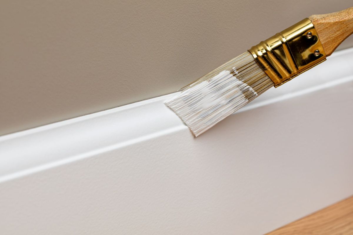 A brush painting a baseboard trim.