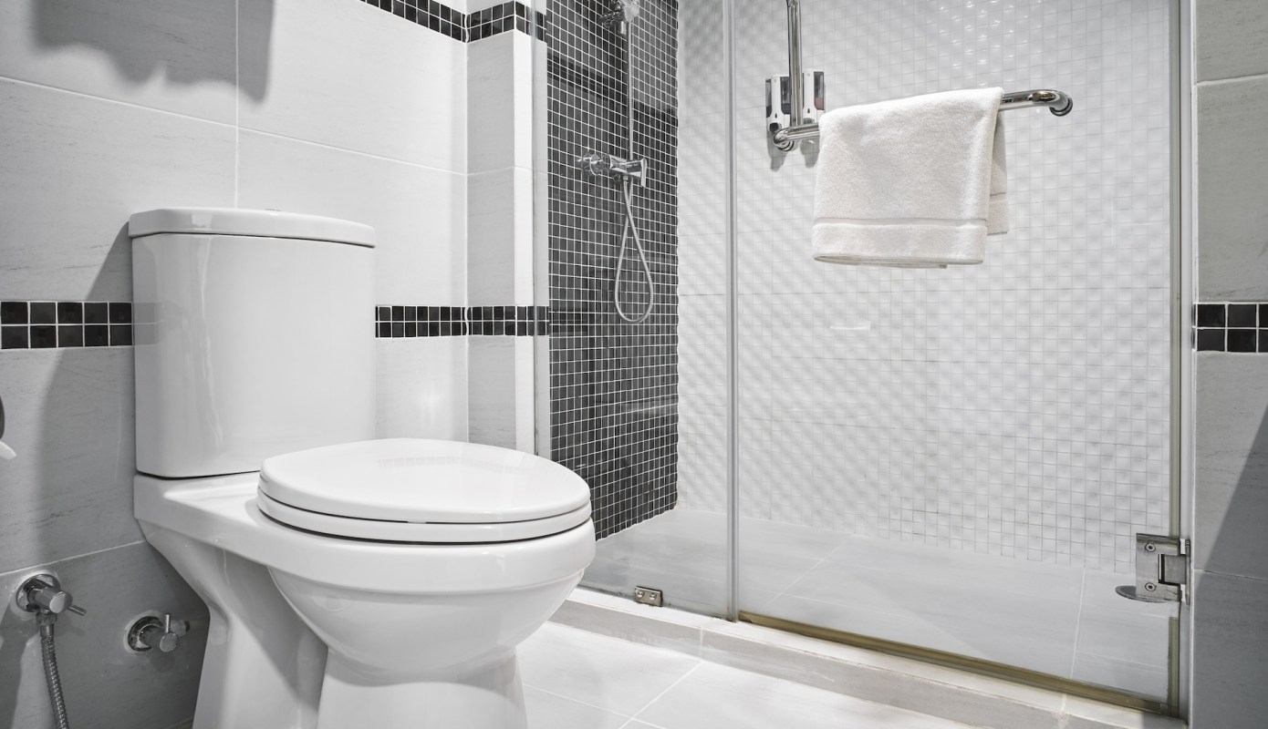 A modern bathroom featuring a toilet, shower, and towel rack with white and black tiled walls.