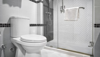 A modern bathroom featuring a toilet, shower, and towel rack with white and black tiled walls.