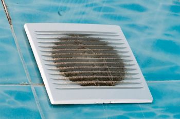 A dirty ventilation grating resting on a blue tiled surface.