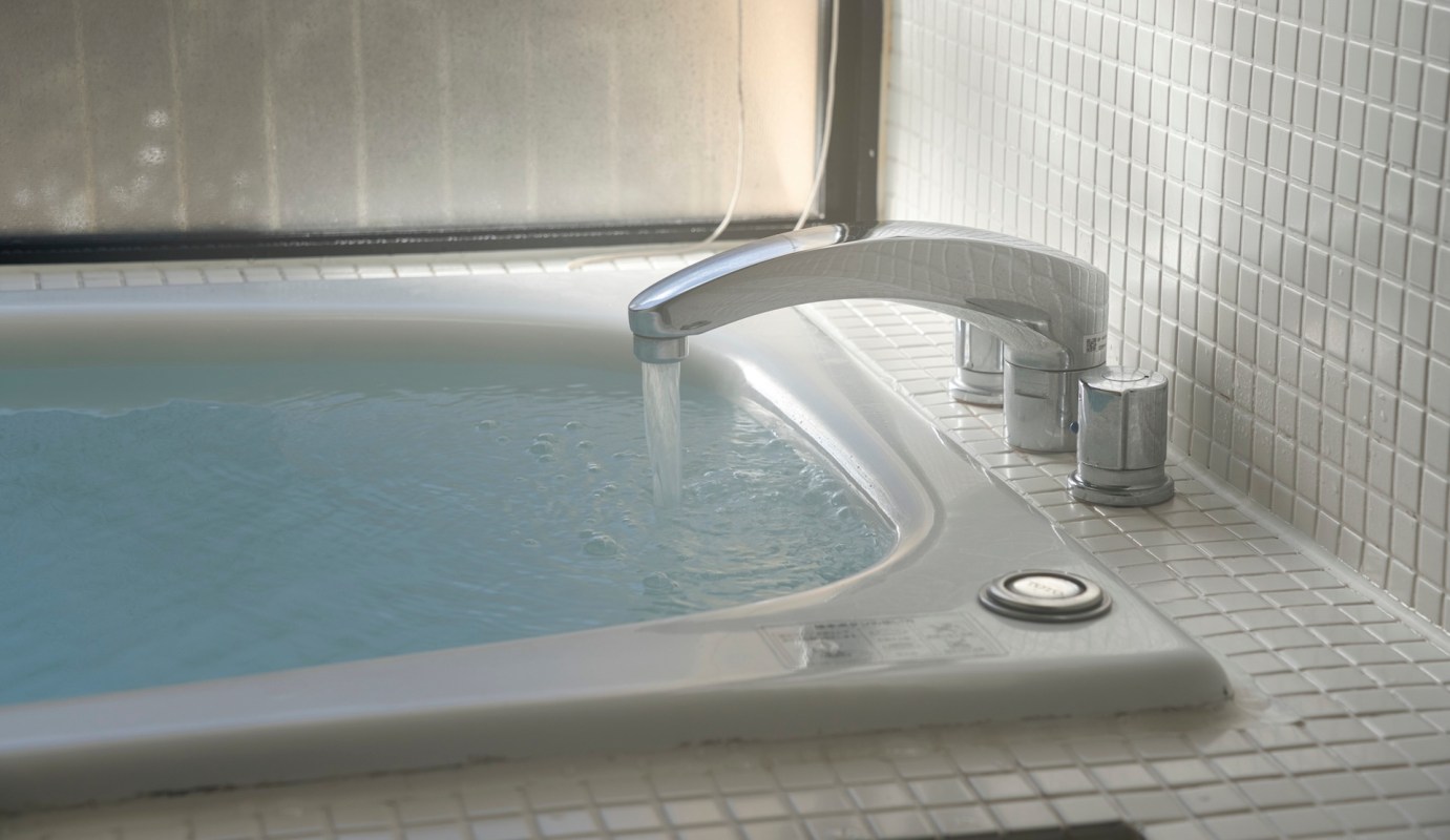 A faucet pouring water into a bathing tub in a tiled bathroom.