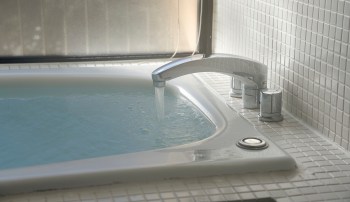 A faucet pouring water into a bathing tub in a tiled bathroom.