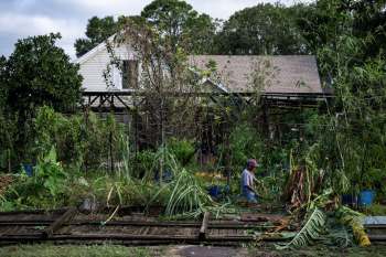 A man works near a storm damaged house with plant debris everywhere